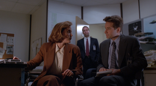 Mulder and Scully exchange a look while Jerry waits in the background.
