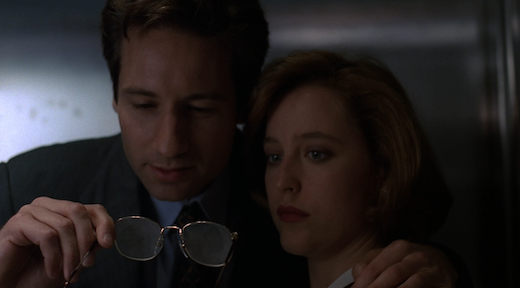 Mulder puts an arm around Scully and pulls her in to show her that he took two fingerprints from one of the ruffians on the surface of his eyeglasses.