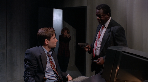 Mulder and Peterson argue, neither seeing that Scully has just walked in with her gun raised.