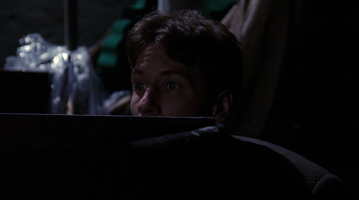 The top half of Mulder's face is visible above the ledge he's hiding behind.