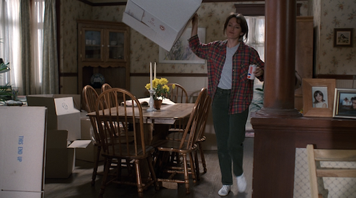 Lauren lifts a box as she walks through her living room.