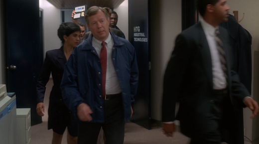 A group of taller agents block Scully from view; only her hand is visible as she lifts her badge.