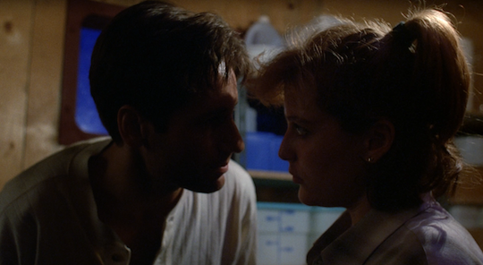 Mulder leans down to speak urgently to Scully.
